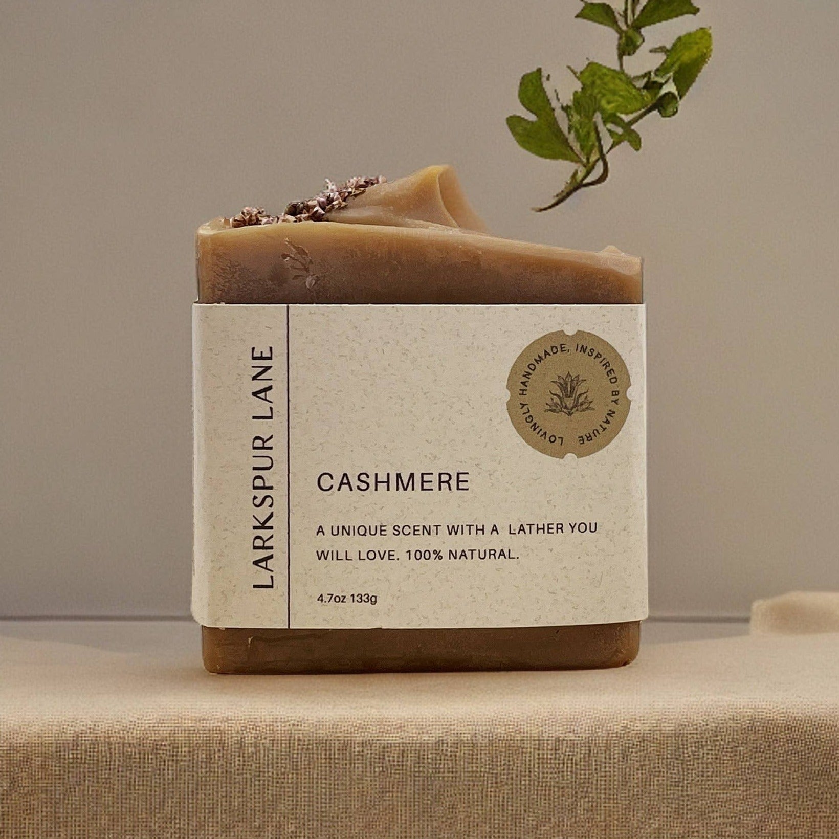 A Larkspur Lane Cashmere Soap Bar with a label that indicates it is a vegan-friendly, handmade soap with natural ingredients, cold-processed, and not tested on animals.