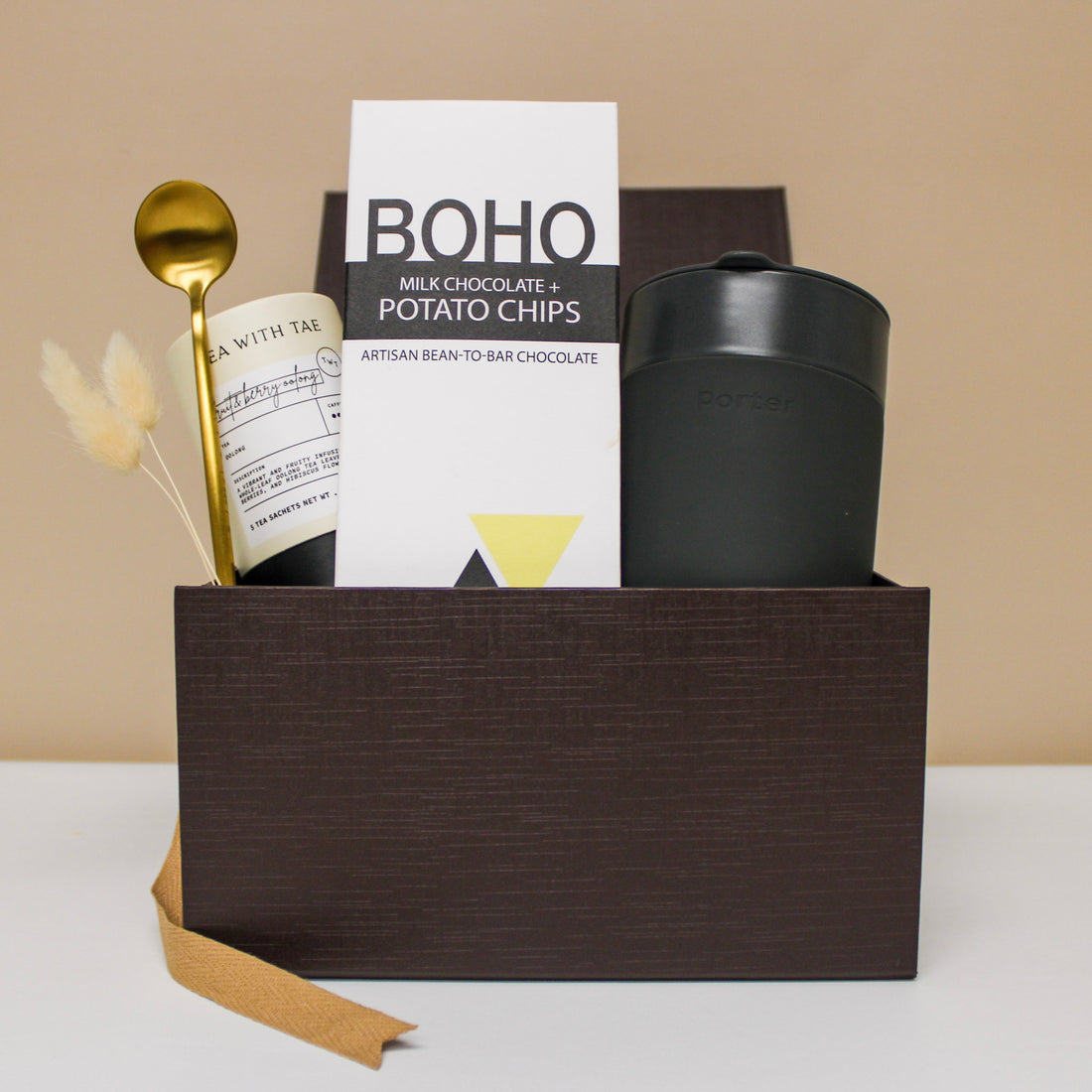 Wellness gift box with travel mug, tea, spoon, and chocolate bar.