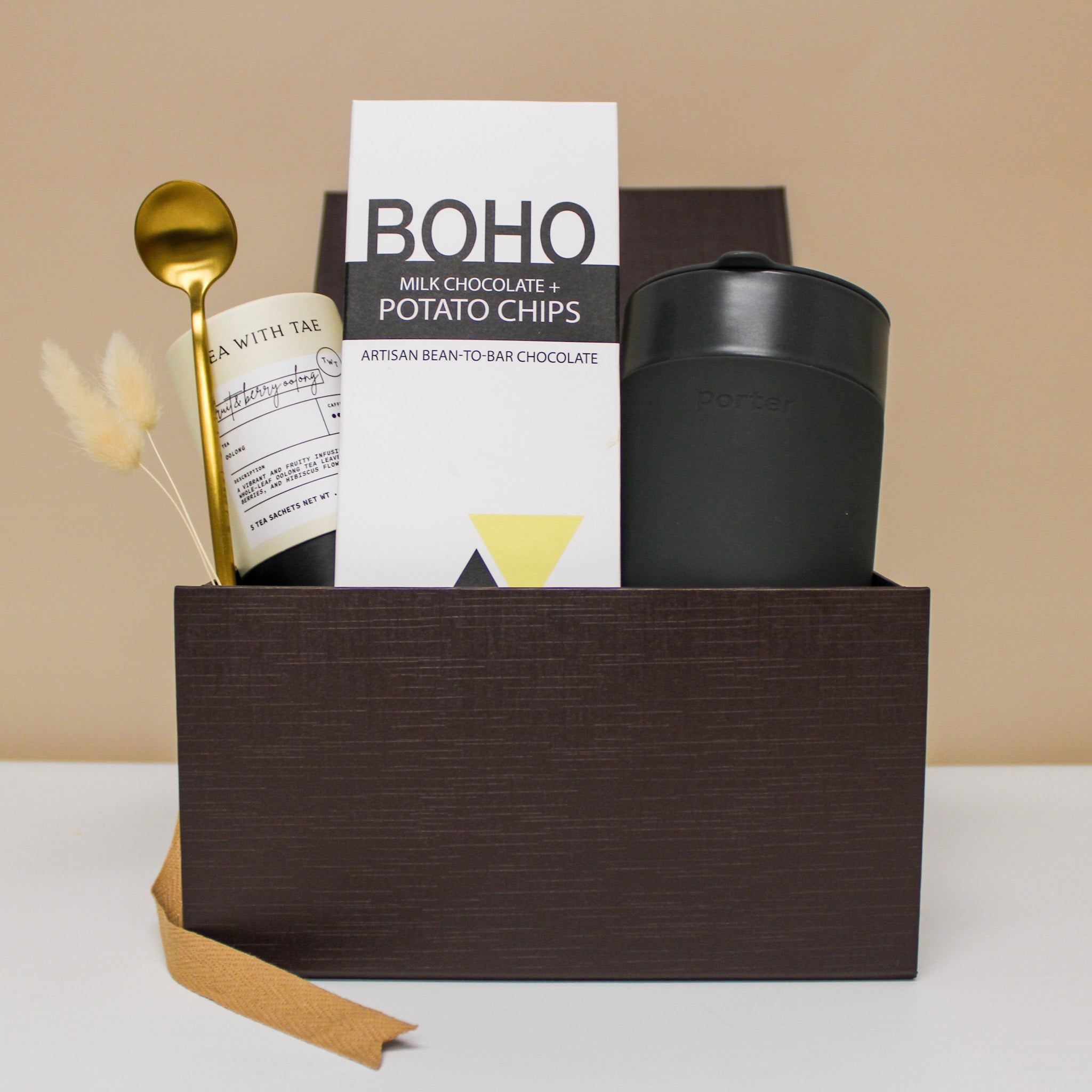 Wellness gift box with travel mug, tea, spoon, and chocolate bar.